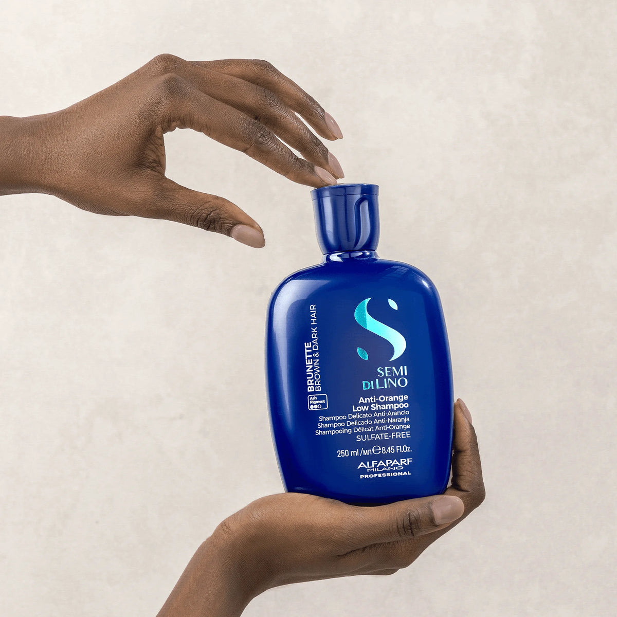 Alfaparf Brunette Anti-Orange Low Shampoo 250ml sostenido en manos, matizador azul para cabello castaño y oscuro.