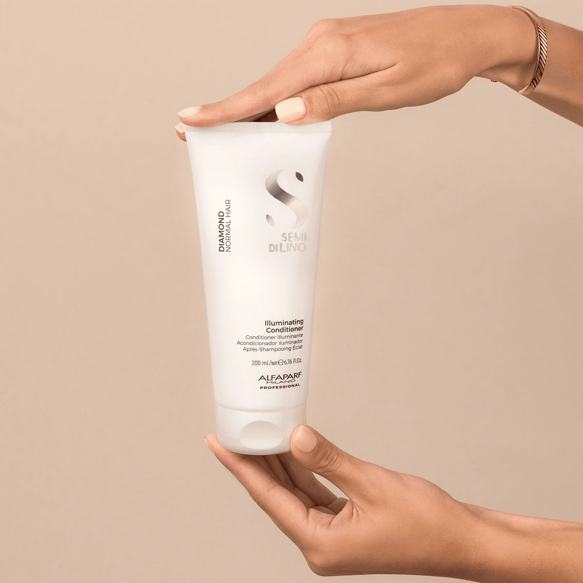 Envase de Alfaparf Semi di Lino Diamond Illuminating Conditioner 200 ml sostenido entre las manos, acondicionador para brillo y desenredado.