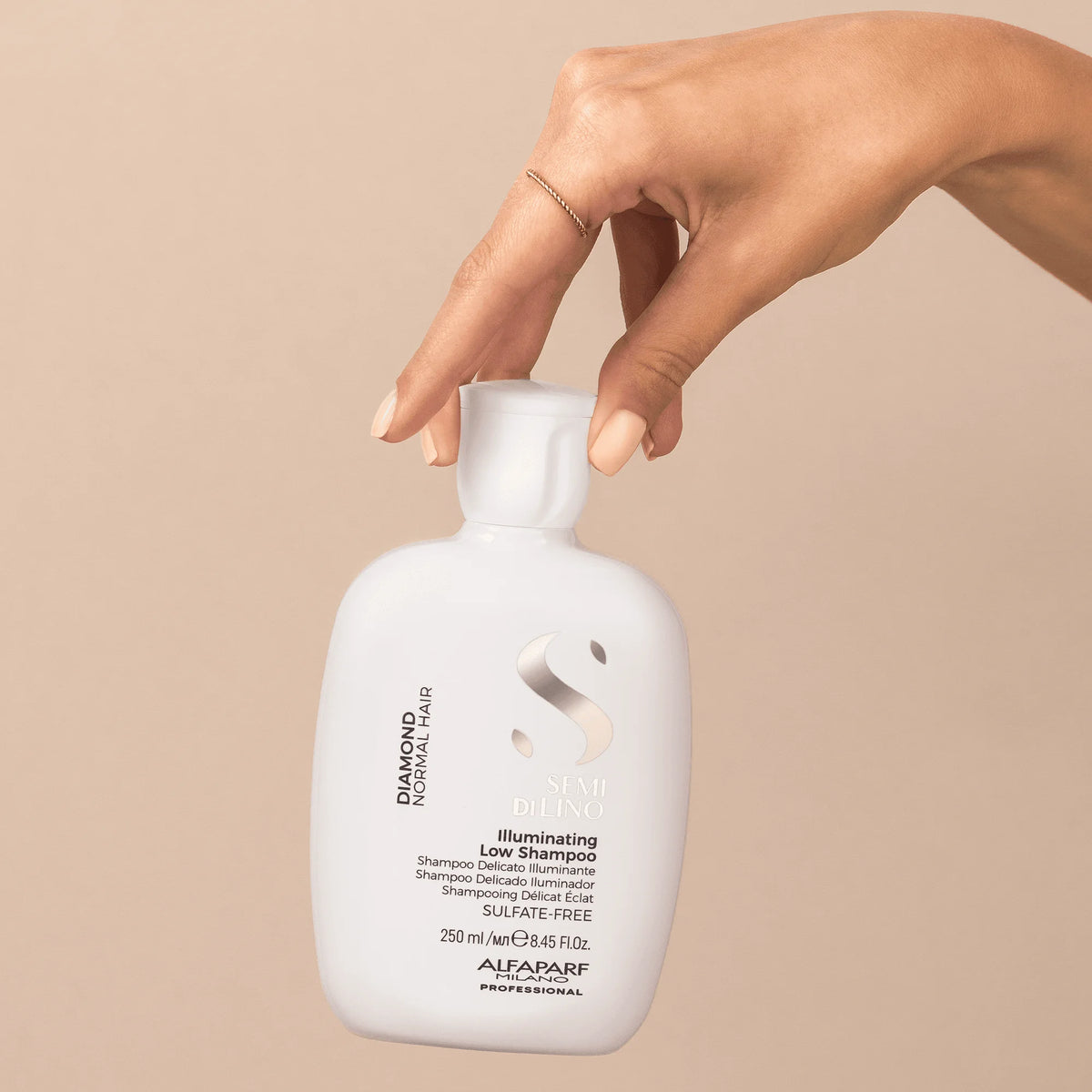 Envase de Alfaparf Semi di Lino Diamond Illuminating Low Shampoo 250 ml sostenido por una mano, shampoo para brillo y limpieza delicada.