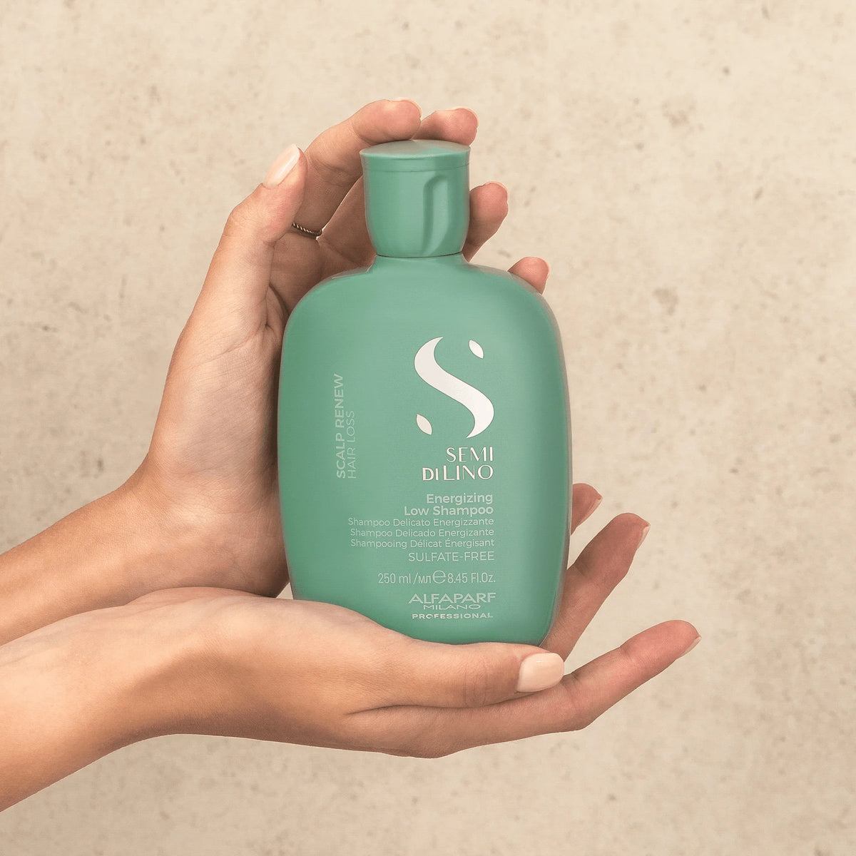 Alfaparf Semi di Lino Energizing Low Shampoo 250 ml sostenido entre las manos, para el cuidado del cabello débil con tendencia a la caída.