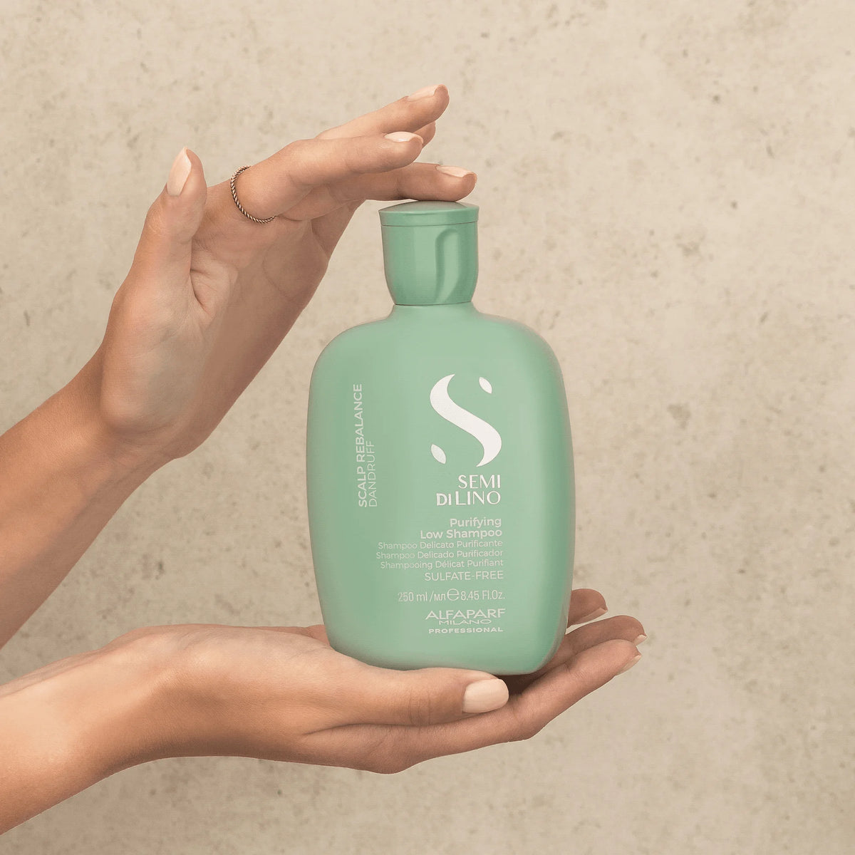 Alfaparf Semi di Lino Purifying Low Shampoo 250 ml sostenido entre las manos, para el cuidado del cuero cabelludo con caspa.
